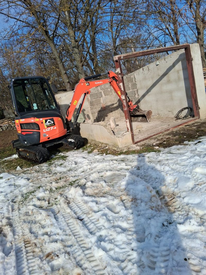 Minibagger beim kontrollierten Abriss eines Nebengebäudes im Winter